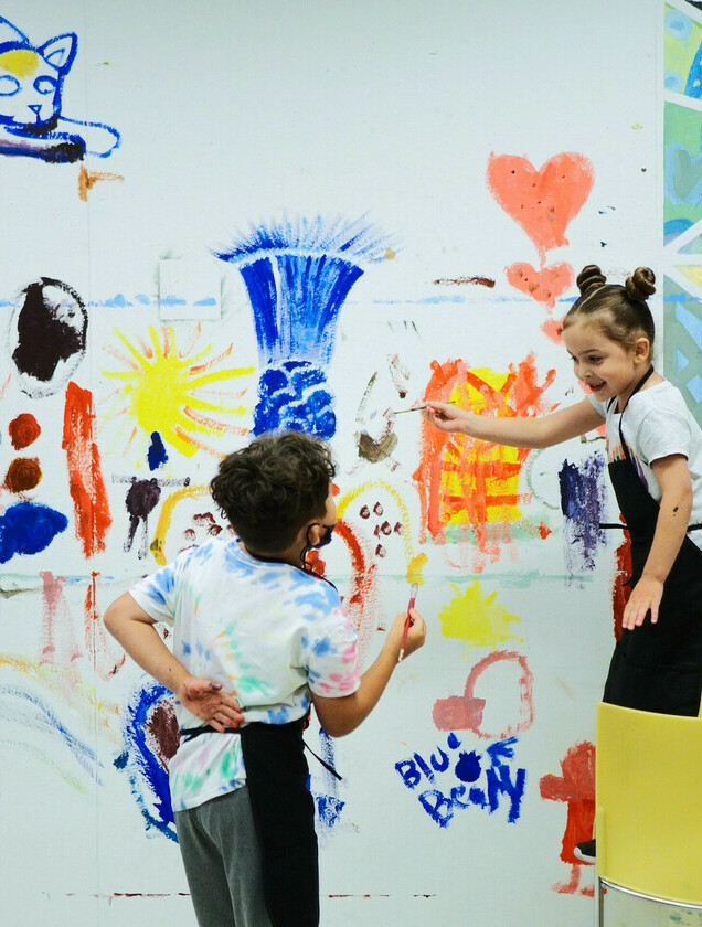 Two young children enthusiastically paint a colourful mural in one of our Art Camps.