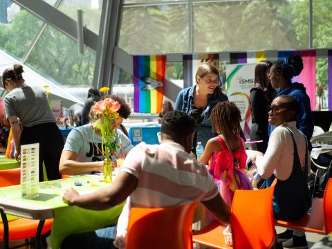 A group of people sit at a table in front of a rainbow banner.